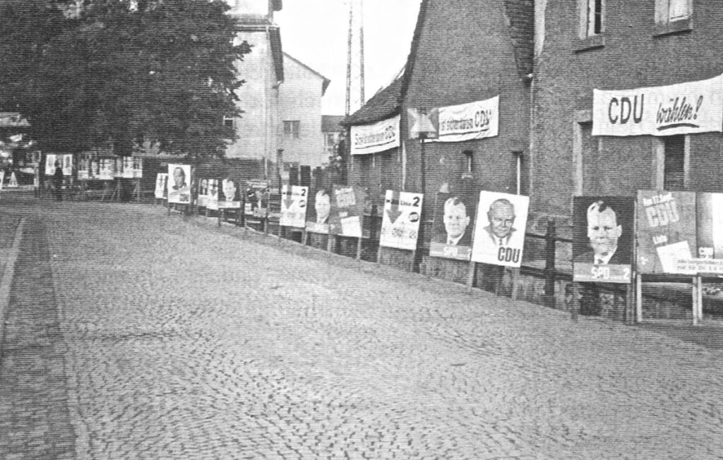 Wahlwerbung. Trinkbrunnenstraße mit der sichtbaren Rodau. Im Hintergrund die Schule.